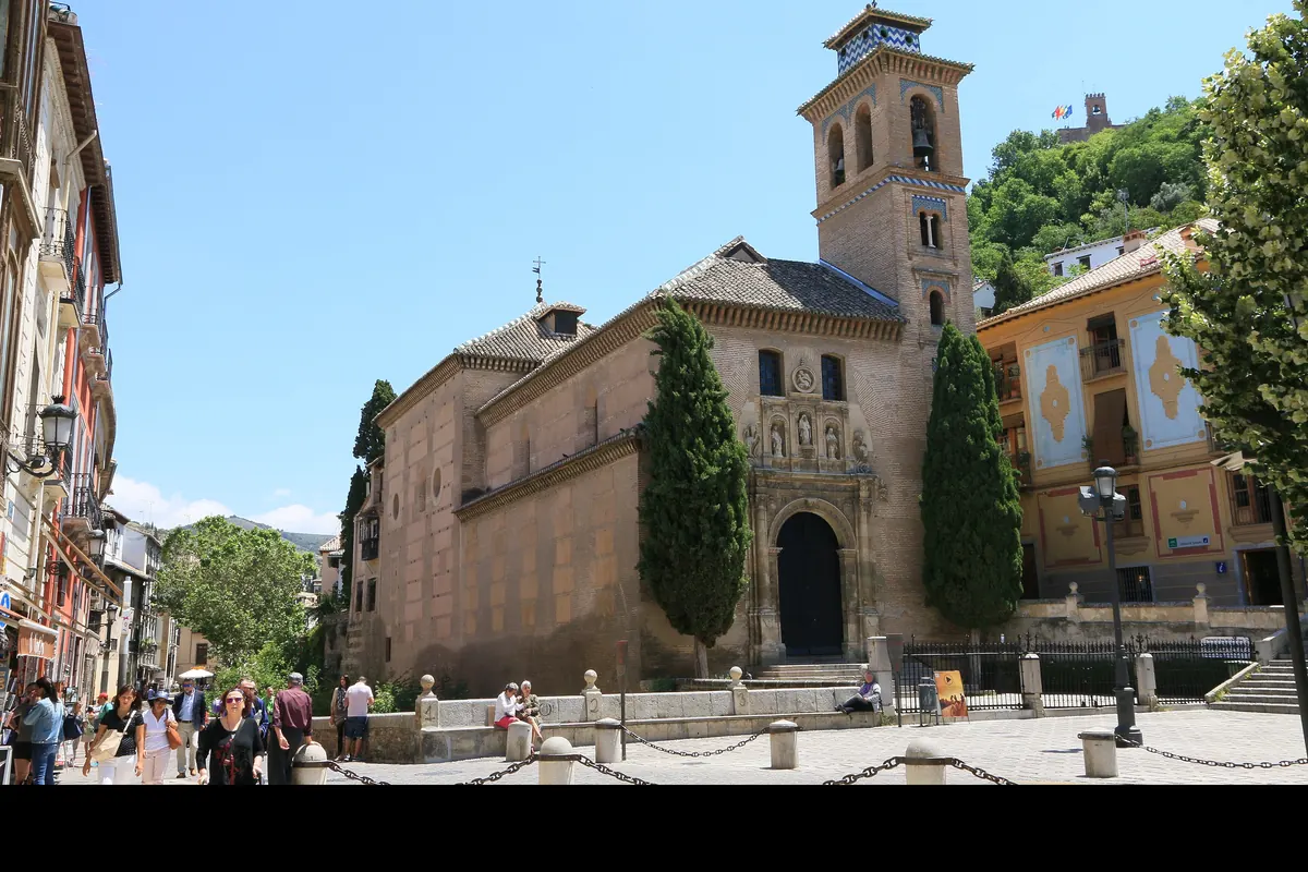 Цегляна дзвіниця та дверний проріз церкви Santa Ana поруч із Plaza Nueva, а позаду, на вкритому деревами пагорбі, — вежа Альгамбри